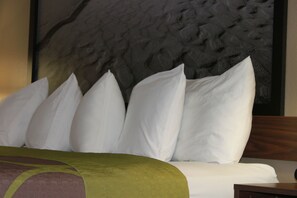 A bed with white pillows and a green bedspread, a wooden headboard, and a textured wall behind. - Super 8 by Wyndham Manistee (Manistee)