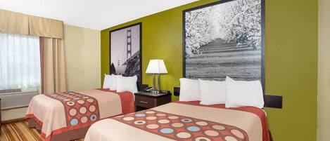 A hotel room with two beds, a window with curtains, a lamp, and artwork on the walls.