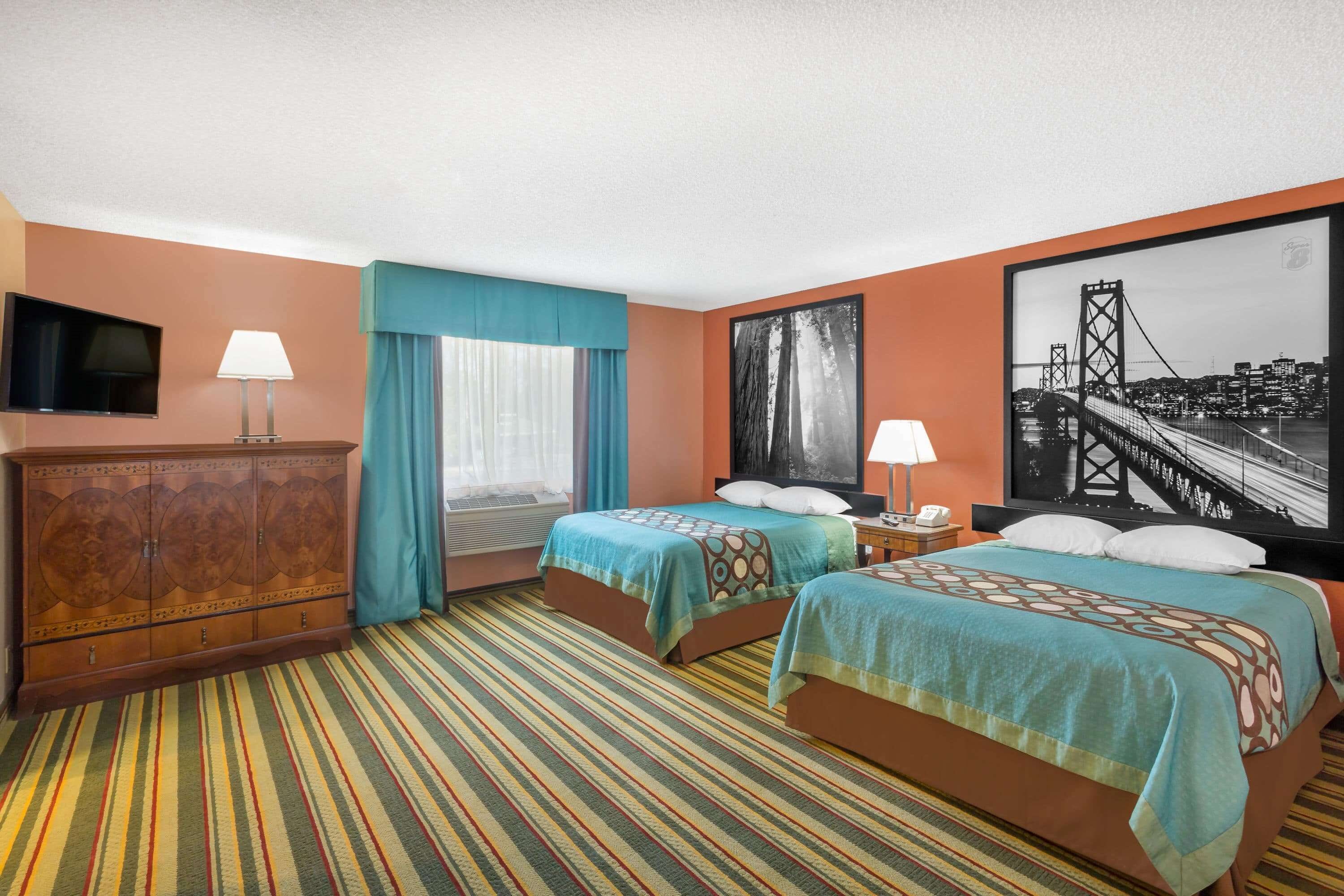 Une chambre d’hôtel avec deux lits, une télévision, une commode et un grand tableau représentant un paysage urbain.