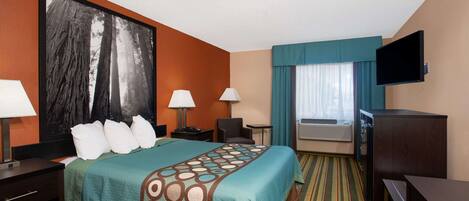 A hotel room with a large bed, two bedside tables with lamps, a desk, a television, and a window with curtains.