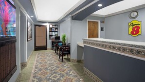 Zona de recepción de hotel con suelo de baldosas, mostrador de recepción, un reloj y un cartel en la pared.