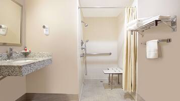 A bathroom with a sink, mirror, towel rack, shower, and a small table.