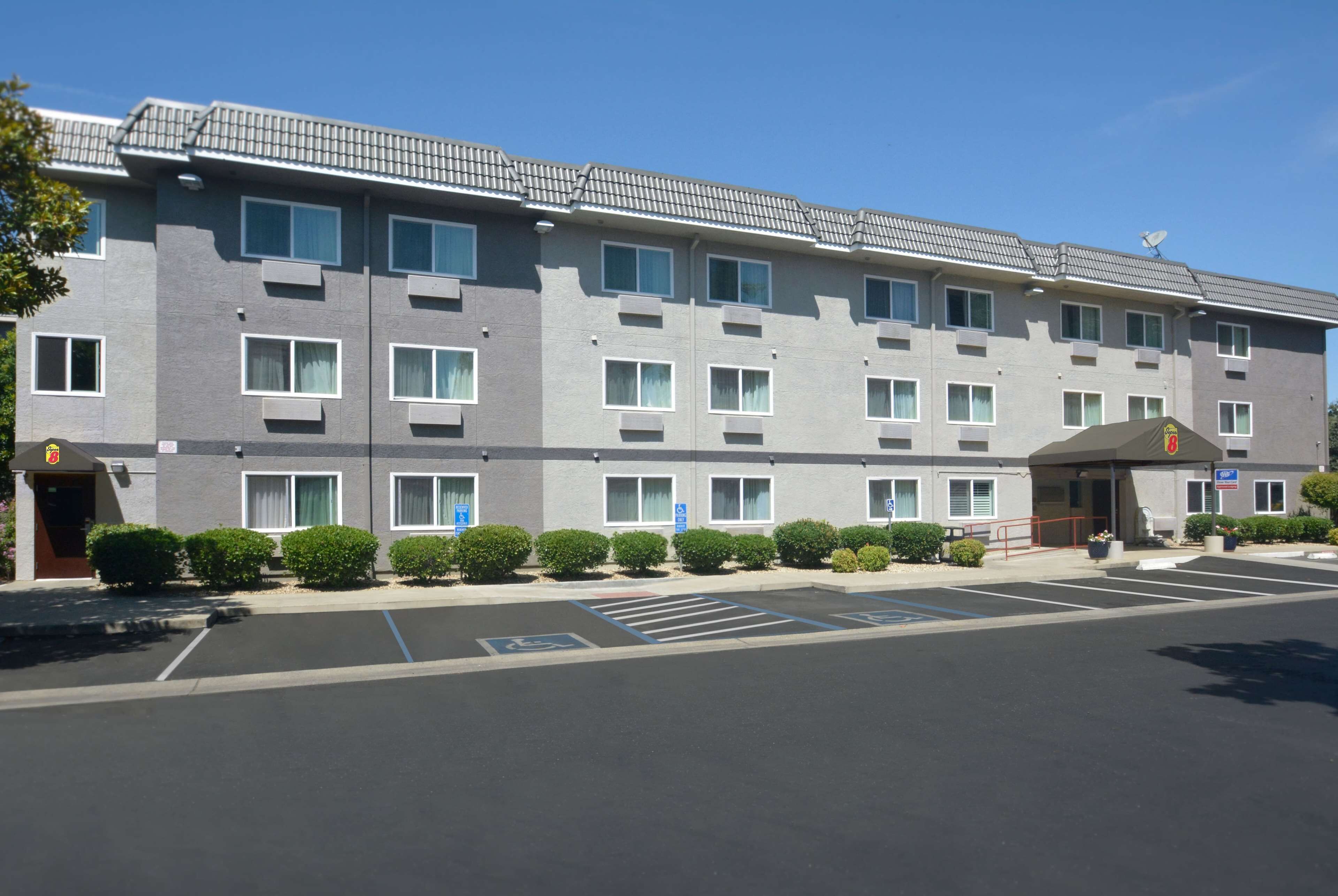 A multi-story hotel with a grey facade, multiple windows, and a parking lot with marked spaces.