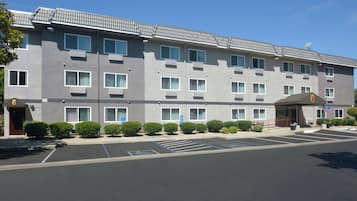 A multi-story hotel with a grey facade, multiple windows, and a parking lot with marked spaces.