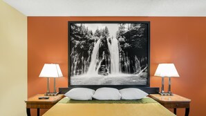 Habitación de hotel con una cama, dos mesitas de noche, un cuadro grande de una cascada en la pared y dos lámparas.