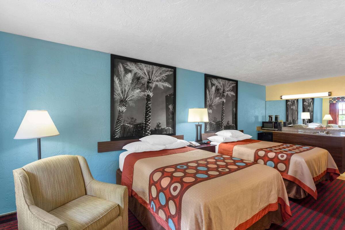 A hotel room with two beds, a chair, a desk, a lamp, and a large mirror.