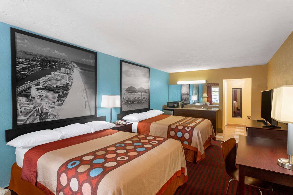 A hotel room with two beds, a desk, a TV, and a bathroom visible in the background.