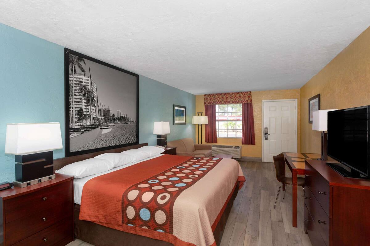 A hotel room with a bed, a desk, a TV, and a window with curtains.