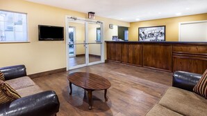 A lobby with a reception desk, a television, a glass door leading outside, and two leather sofas.