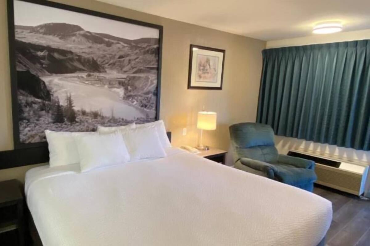 A hotel room with a large bed, a chair, a desk, a lamp, and a picture on the wall.