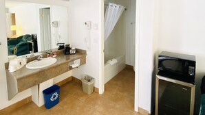 A bathroom with a sink, mirror, shower, and a microwave.
