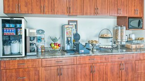 A kitchen with wooden cabinets, a coffee machine, a waffle maker, and various food items on the counter.