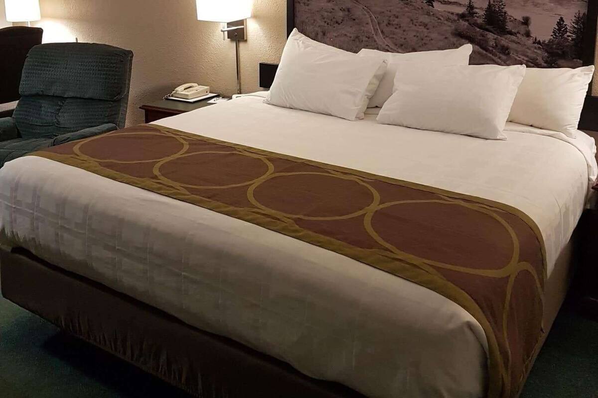 A hotel room with a large bed, a chair, a nightstand with a phone, and a lamp.