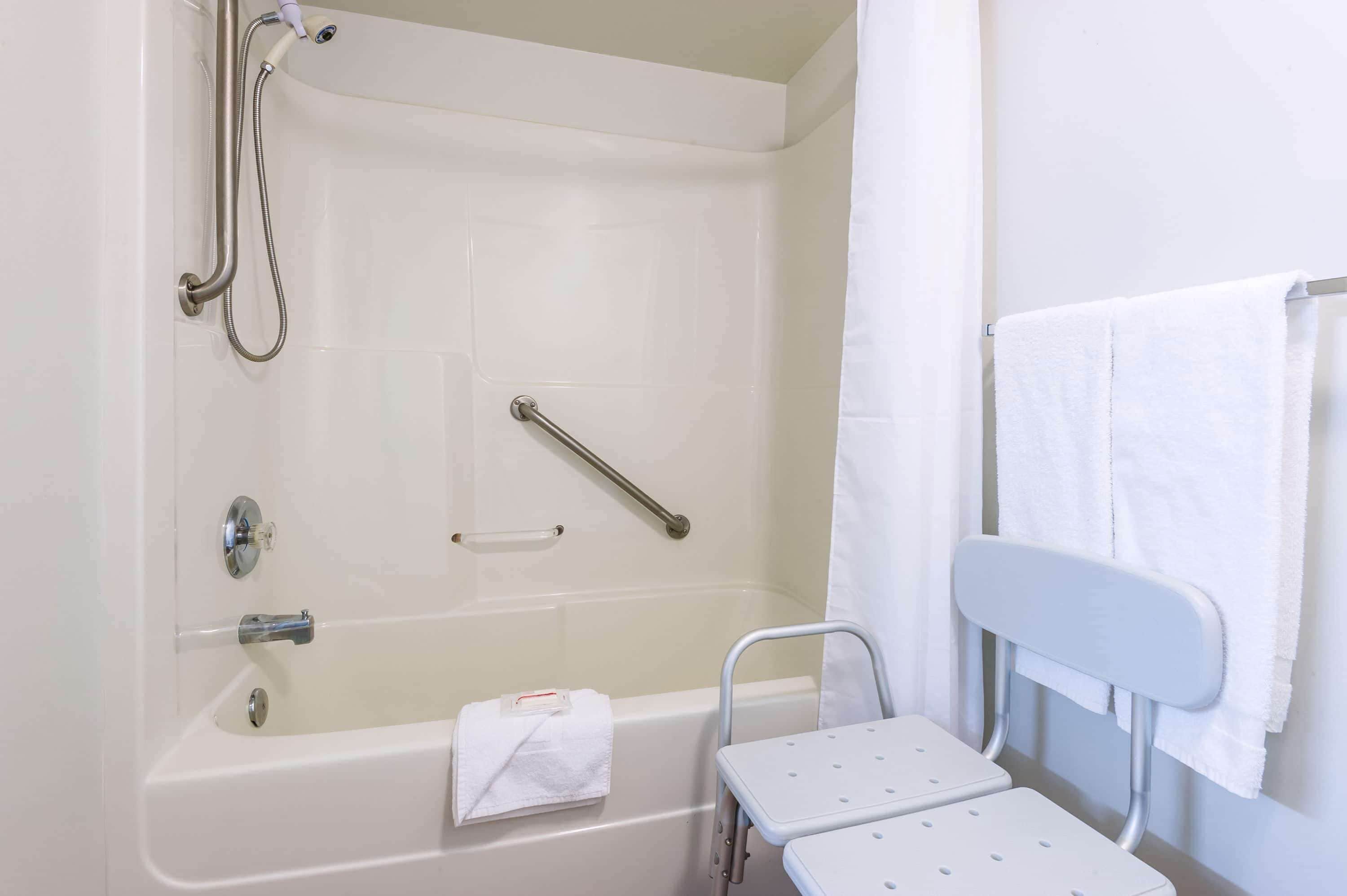 A bathroom with a bathtub, a shower, a grab bar, a white towel, and a small table.