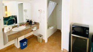 A bathroom with a sink, mirror, towel dispenser, and a shower curtain.