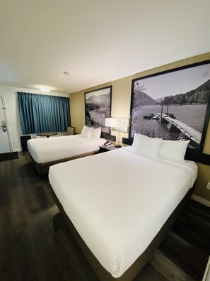 Habitación de hotel con dos camas, un escritorio, una silla, una lámpara y un ventanal con vistas a un lago y montañas.