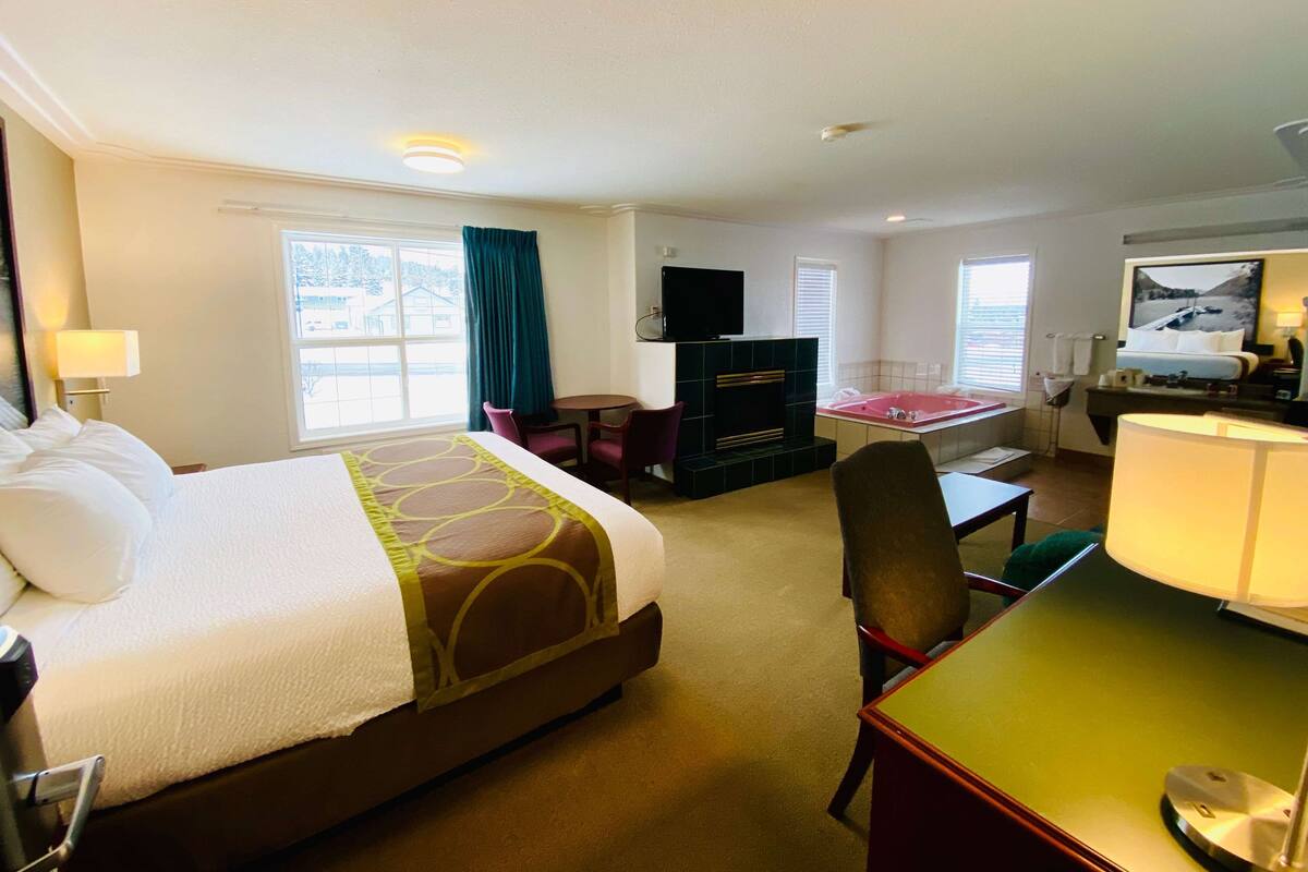 A hotel room with a large bed, a desk, a chair, a TV, and a bathtub.