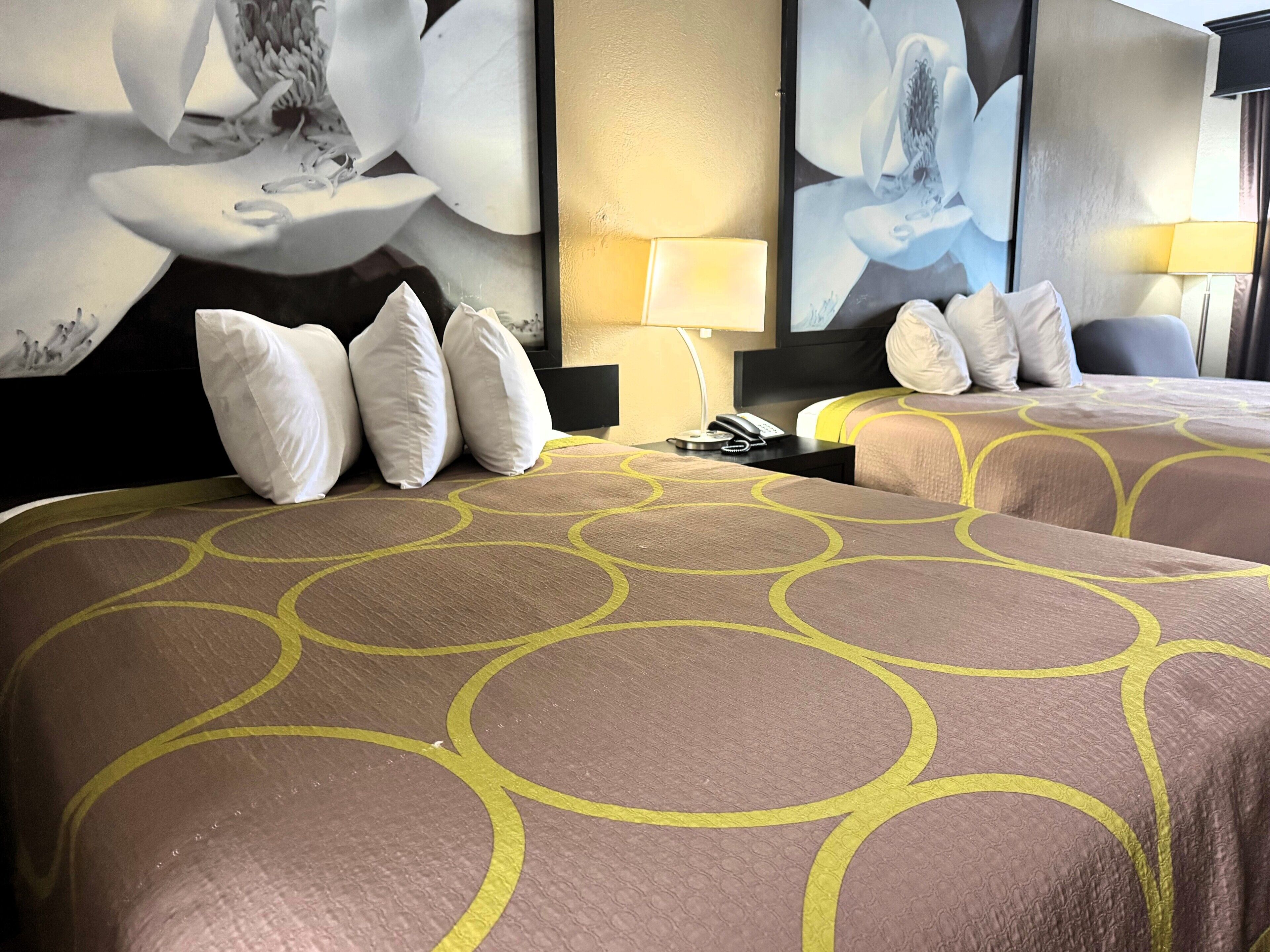 Una habitación de hotel con dos camas, cada una con una colcha estampada, una mesita de noche con lámpara y una pared decorada con motivos florales.