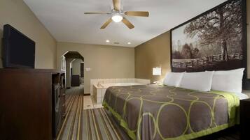 A hotel room with a bed, a television, a ceiling fan, and a painting on the wall.