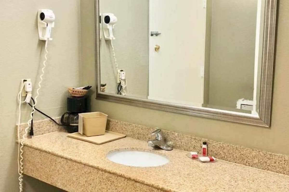A bathroom with a sink, mirror, hair dryer, and coffee maker.