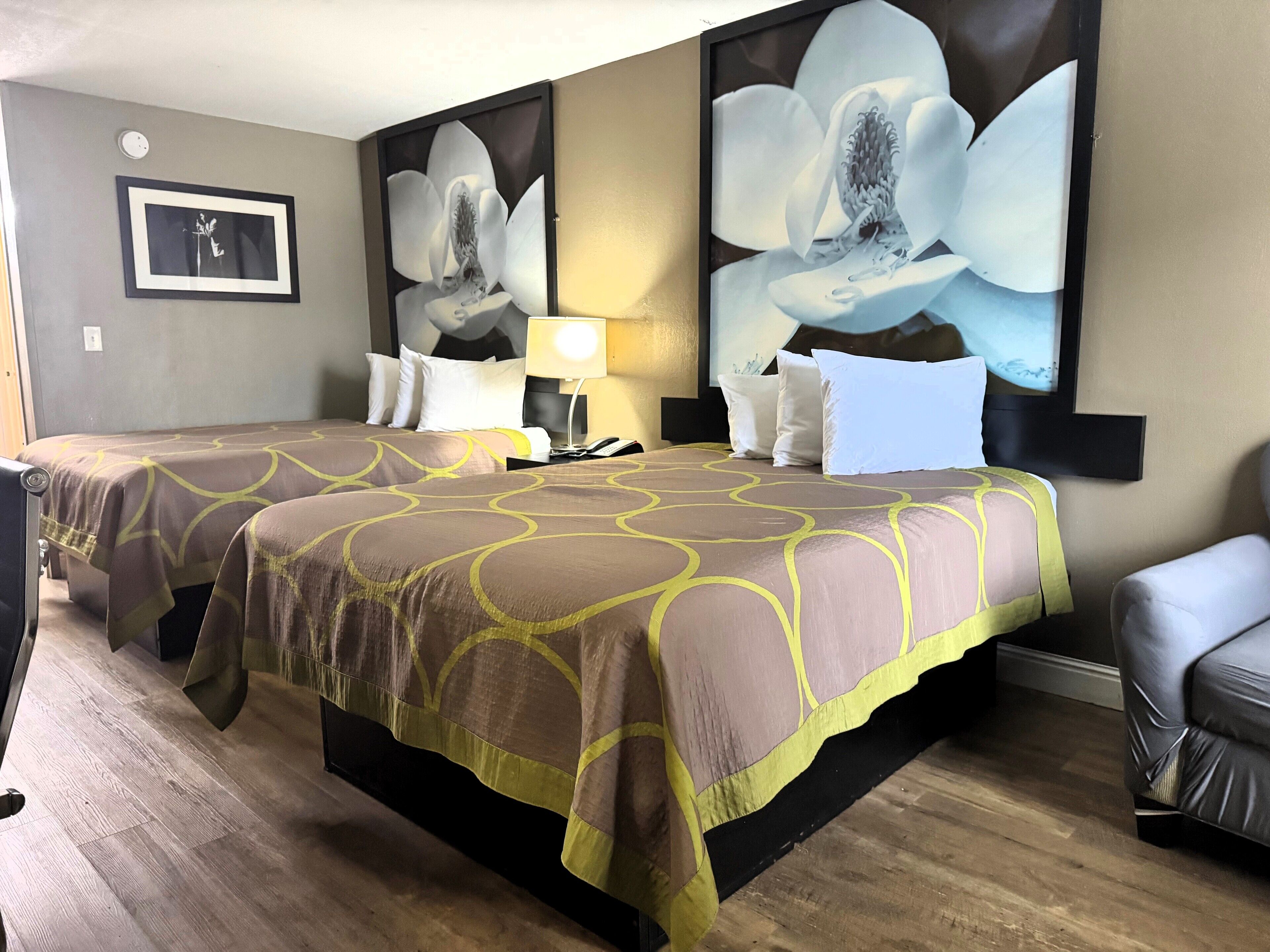 Habitación de hotel con dos camas, una mesita de noche, una lámpara y un cuadro grande con flores en la pared.