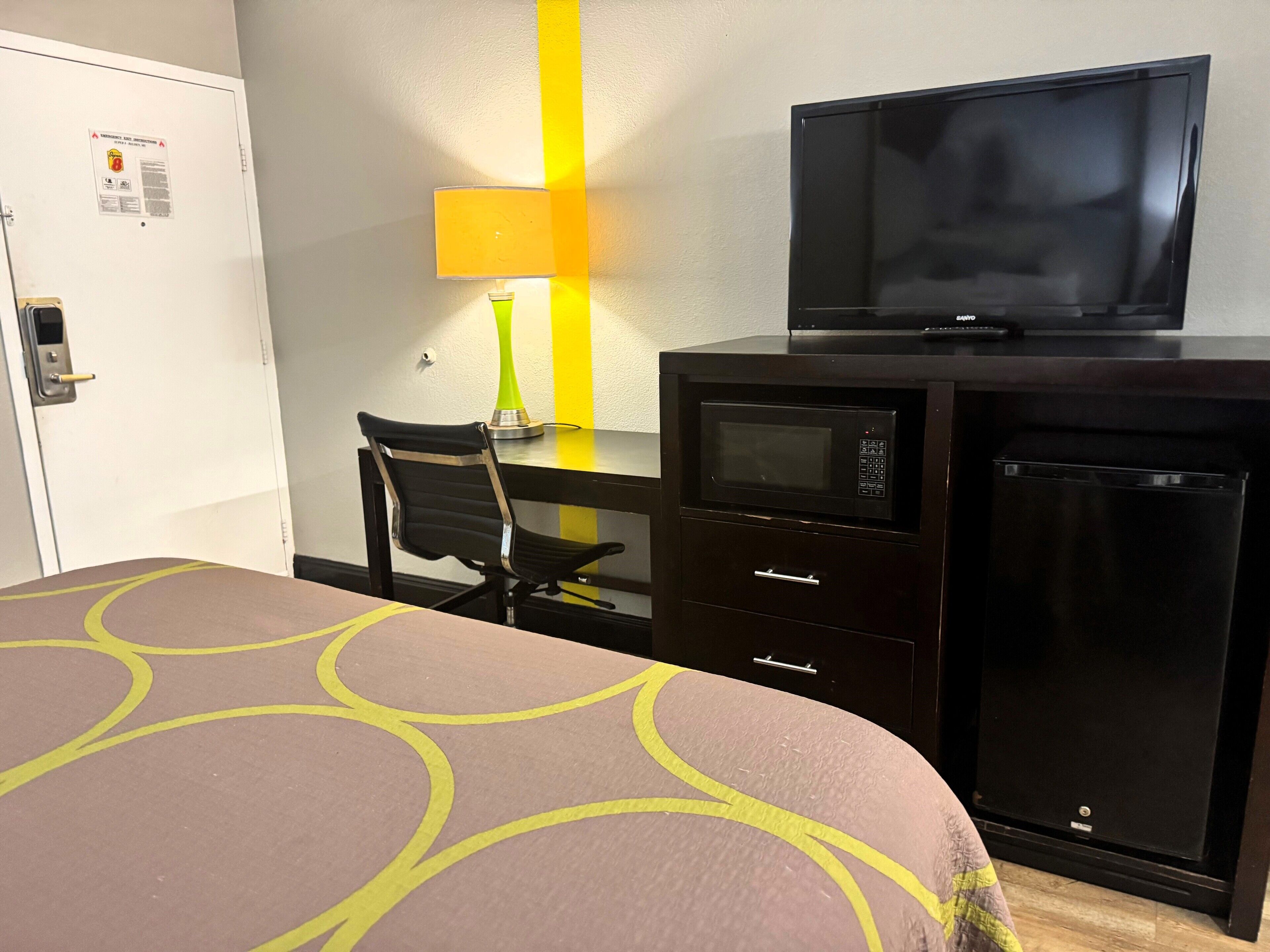 A hotel room with a bed, a desk with a TV, a microwave, and a refrigerator.
