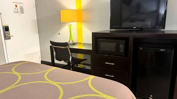 A hotel room with a bed, a desk with a TV, a microwave, and a refrigerator.