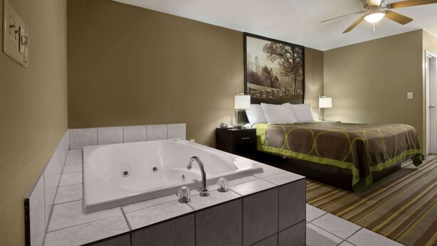 Een hotelkamer met een groot bad, een bed met een groenbruine plaid, een nachtkastje met een lamp en een plafondventilator.