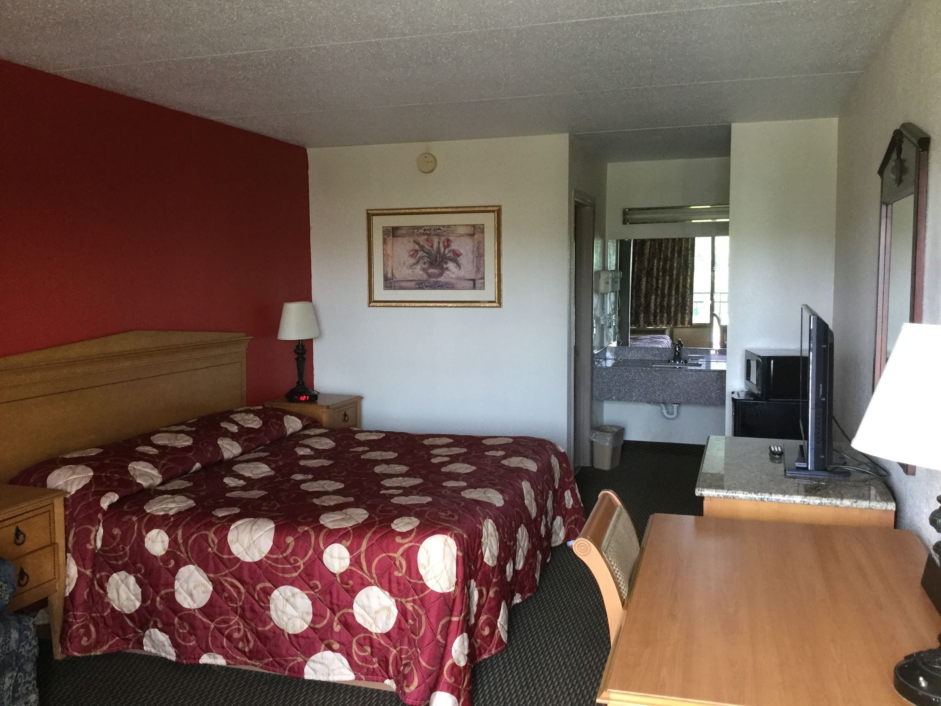 A hotel room with a large bed, a desk, a television, and a bathroom visible through an open door.