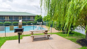 A swimming pool area with a picnic table and grill, surrounded by a fence and greenery. - Americas Best Value Inn Goodlettsville Nashville N (Goodlettsville)