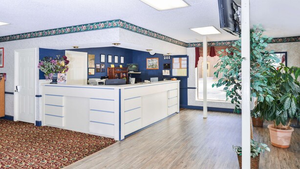 A reception area with a wooden floor, a reception desk, a television, and a bulletin board. - Americas Best Value Inn Goodlettsville Nashville N (Goodlettsville)