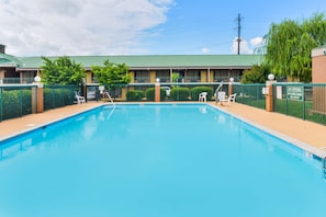 Una piscina con una cerca verde, un edificio con techo verde, y un letrero que dice "NO DIVING NO LIFEGUARD ON DUTY".