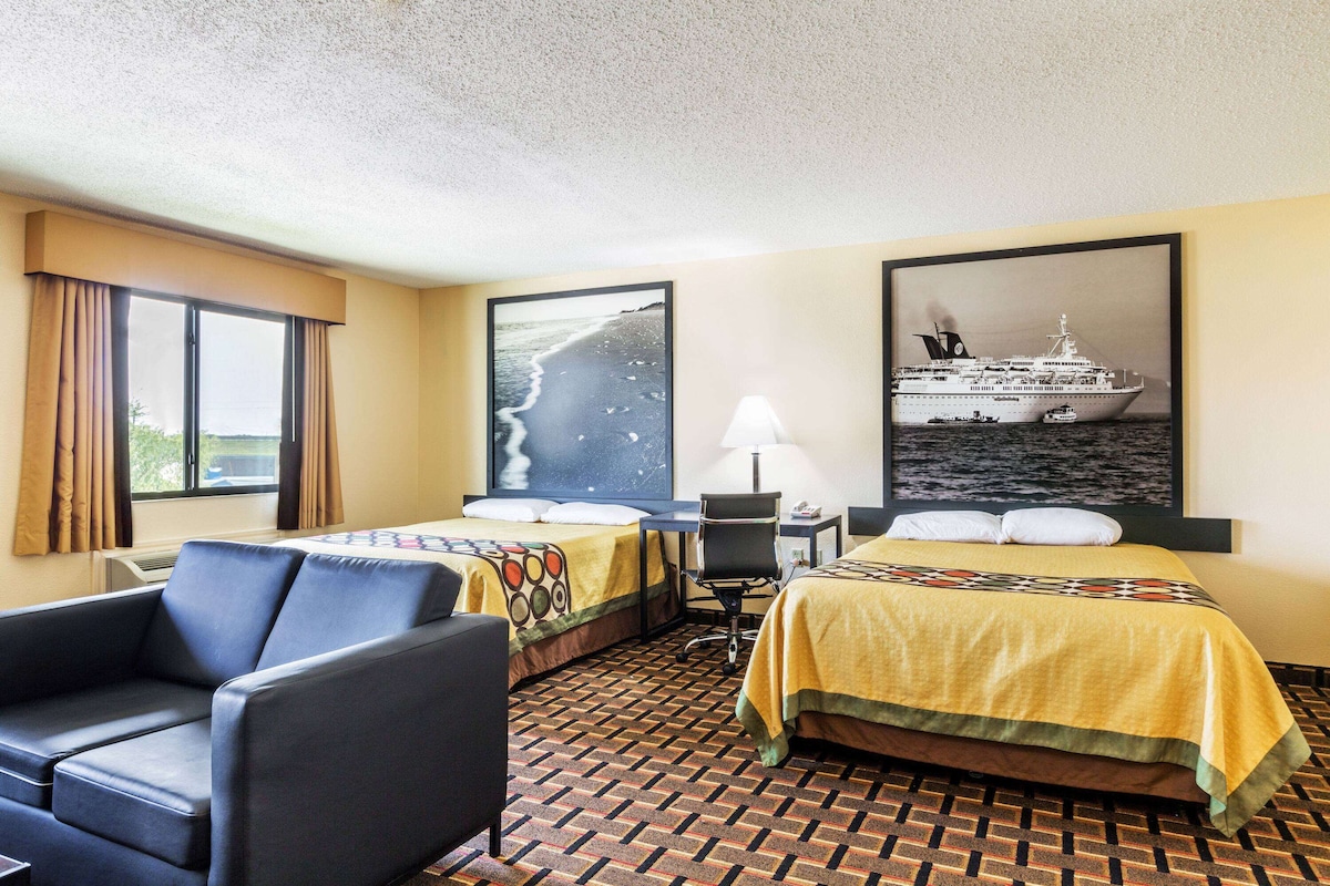 Una habitación de hotel con dos camas, un escritorio, una silla y un ventanal grande.