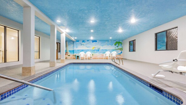 An indoor swimming pool with a mural of a beach scene on the wall, white chairs, and a clear blue pool.