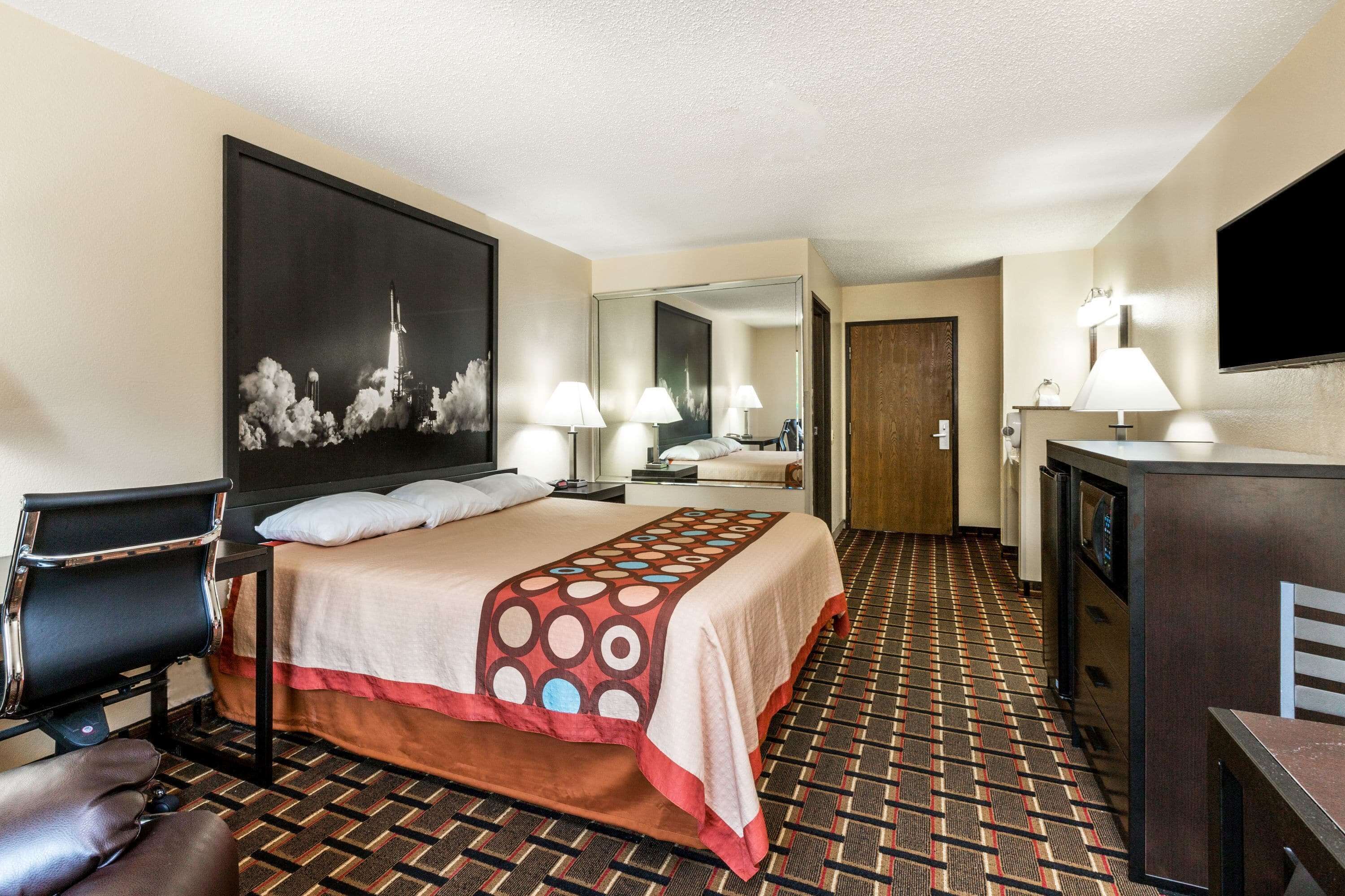 Habitación de hotel con una cama grande, un escritorio, una silla, un televisor y un baño visible a través de una puerta abierta.