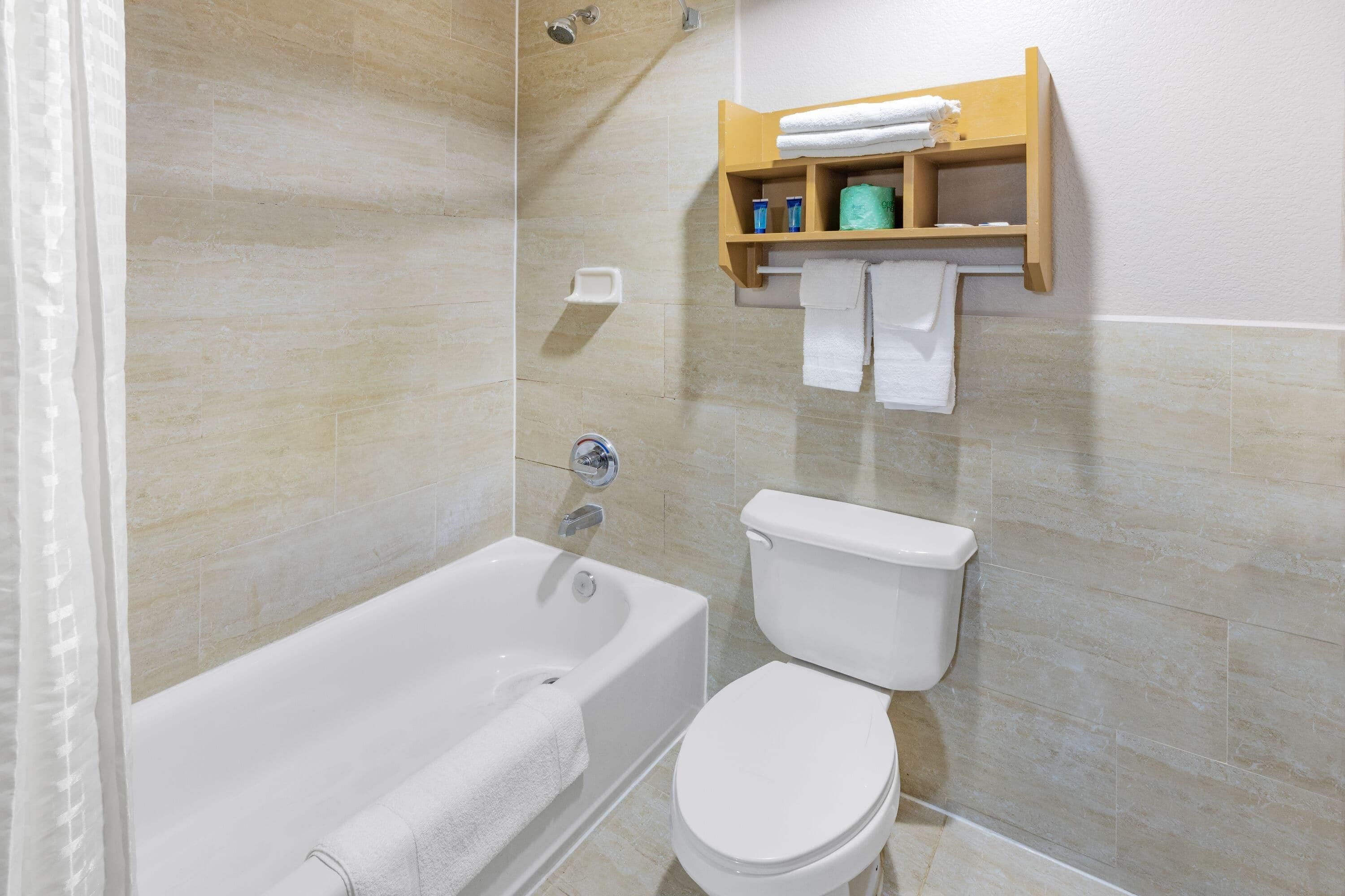Un baño con bañera, inodoro y un estante con artículos de aseo.