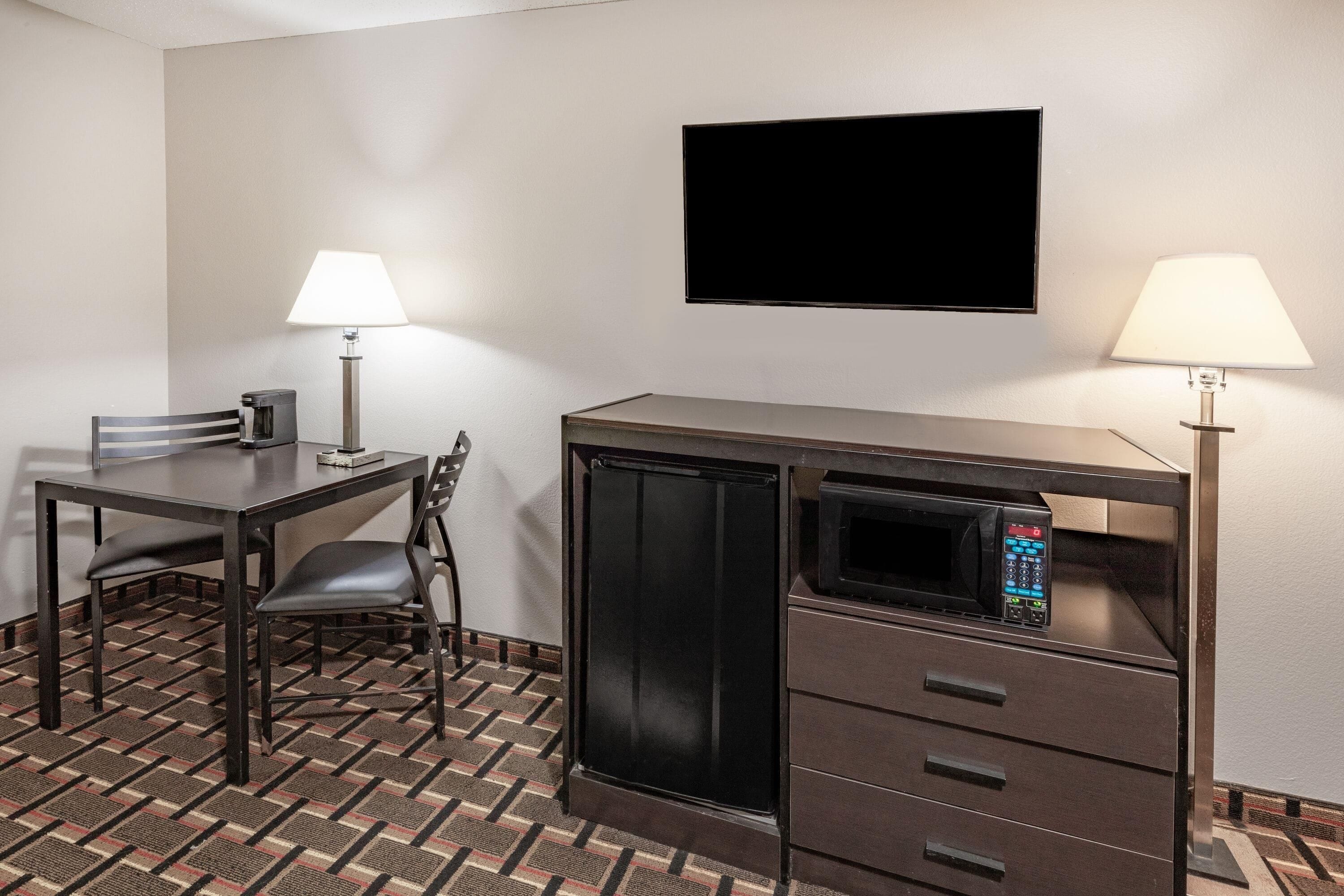 Ein kleines Hotelzimmer mit Bett, Schreibtisch mit Stuhl, einer Mikrowelle, einem Fernseher und zwei Nachttischlampen.
