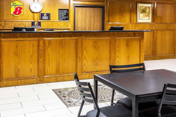 Zona de recepción de un hotel con un mostrador de madera, un reloj y un cuadro en la pared.