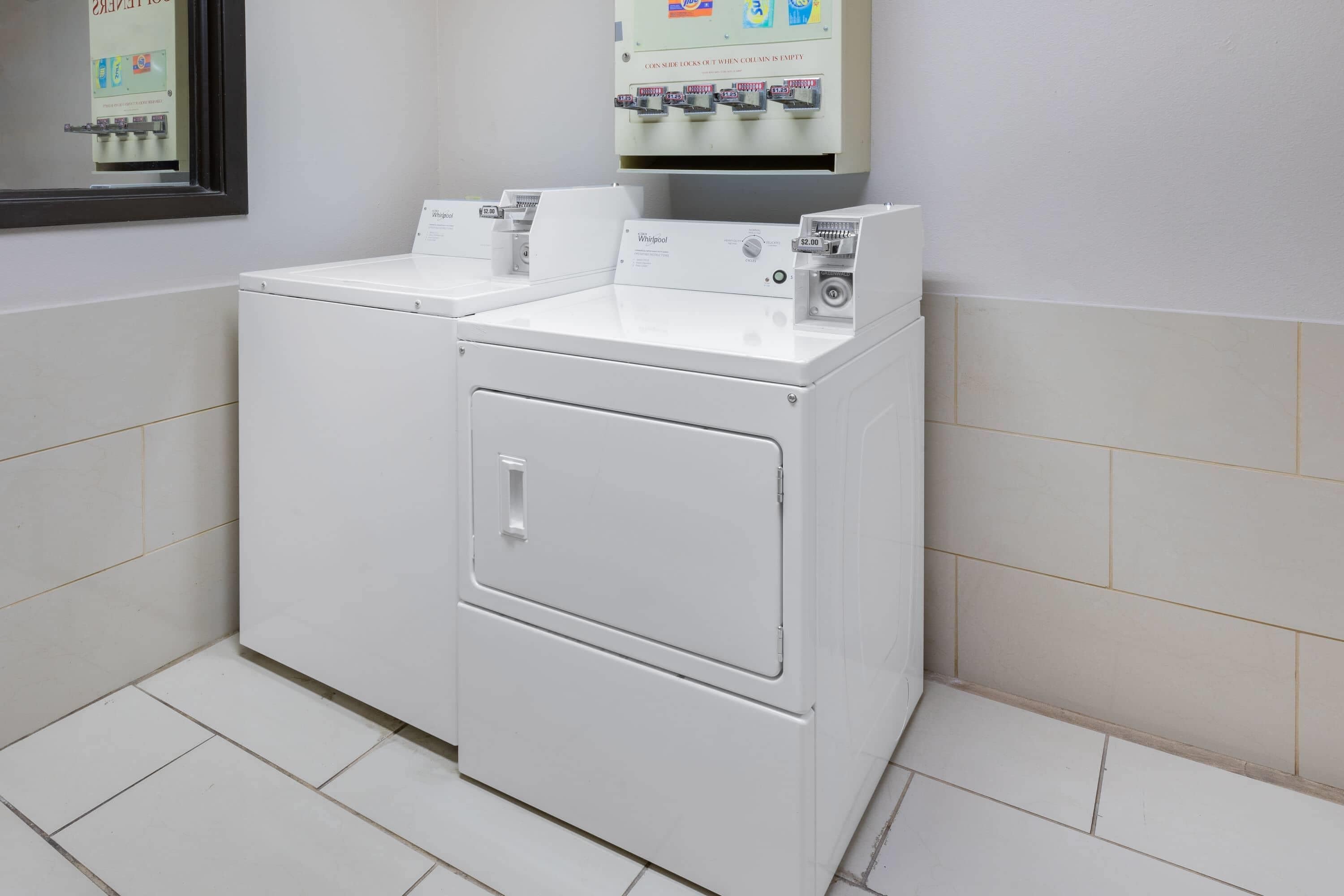 A laundry facility with two Whirlpool washers and dryers, a coin-operated dryer, and a sign indicating a $2.00 fee.