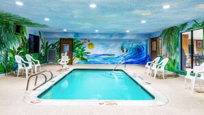 Piscina interior con un mural tropical, sillas de plástico blanco y un letrero que indica que no se permite bucear.