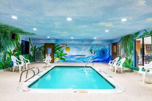 Piscina interior con un mural tropical, sillas de plástico blanco y un letrero que indica que no se permite bucear.