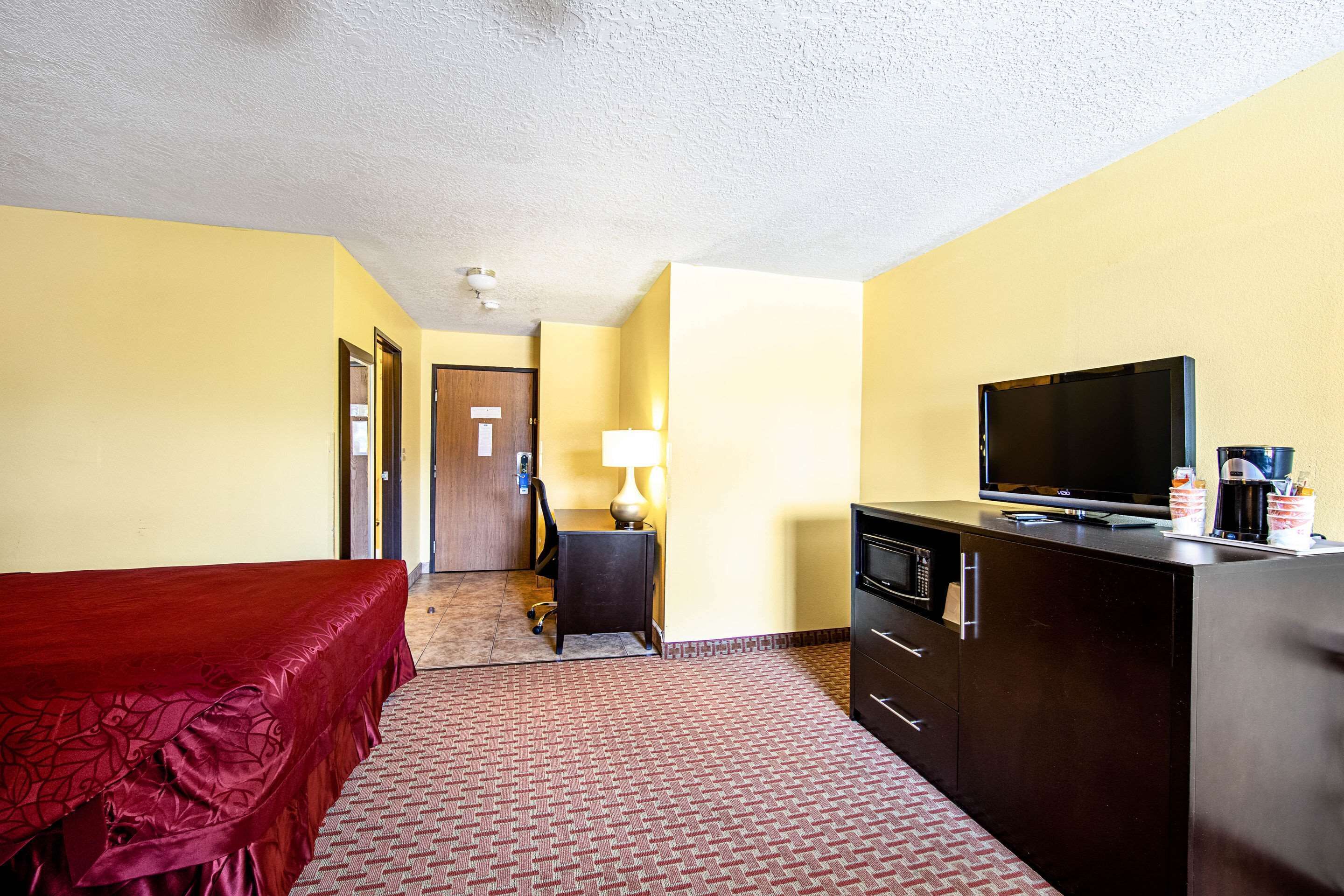Una camera d'albergo con un letto, una scrivania con una lampada, una televisione e un minibar.