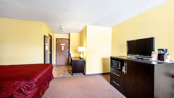 Una camera d'albergo con un letto, una scrivania con una lampada, una televisione e un minibar.