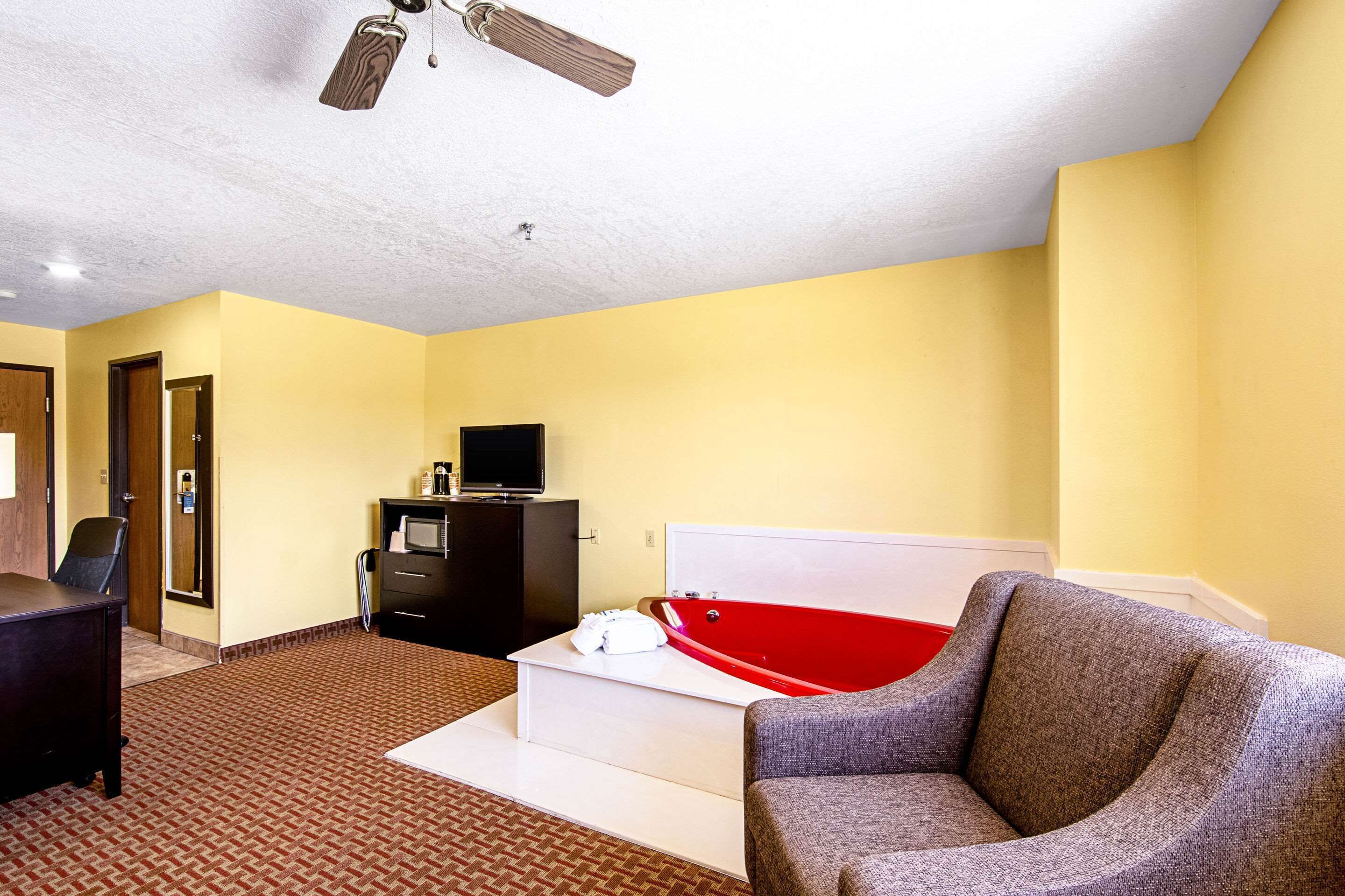 Ein Hotelzimmer mit einer roten Badewanne, einem grauen Sessel, einem Schreibtisch und einem Deckenventilator.