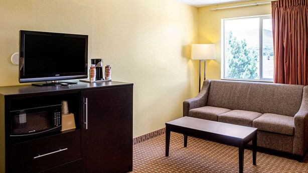 A hotel room with a flat-screen TV on a cabinet, a sofa, a coffee table, and a lamp.