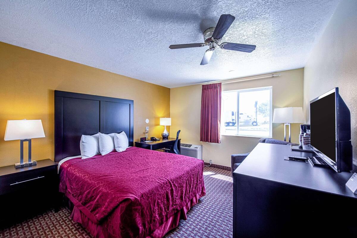 Een hotelkamer met een bed, bureau, plafondventilator en raam met gordijnen.