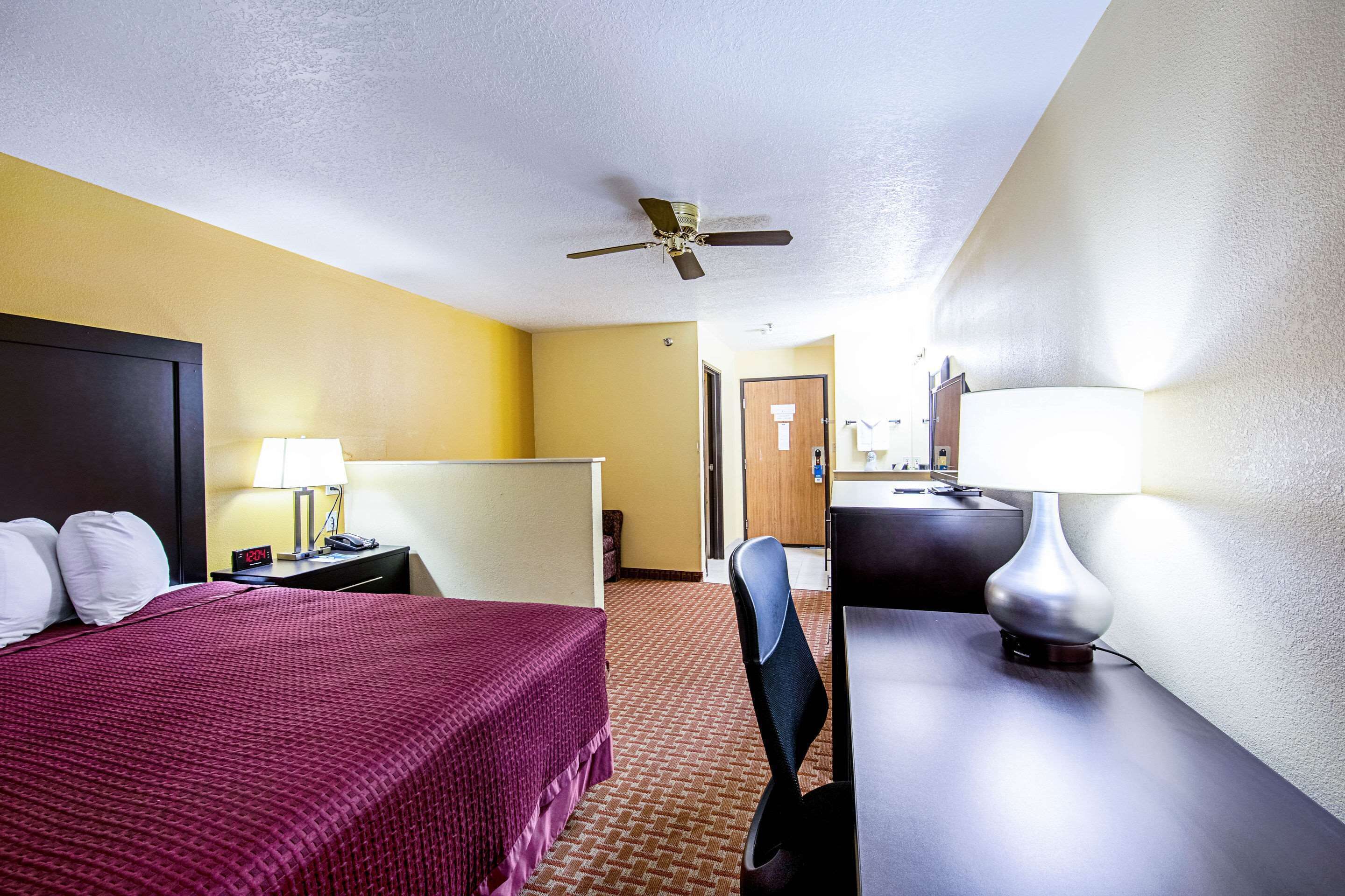 A hotel room with a bed, desk, chair, lamp, and a ceiling fan.