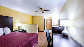 A hotel room with a bed, desk, chair, lamp, and a ceiling fan.