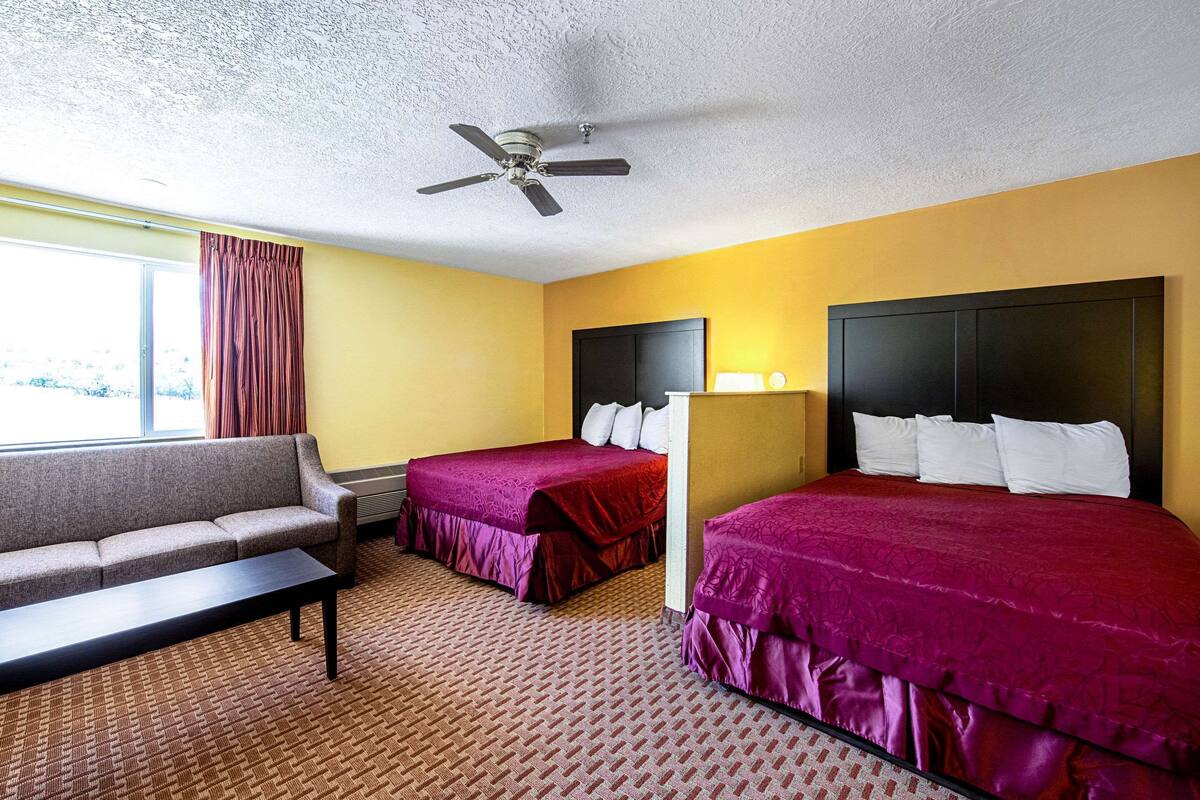 Een hotelkamer met twee bedden, een bank, een bureau en een plafondventilator.