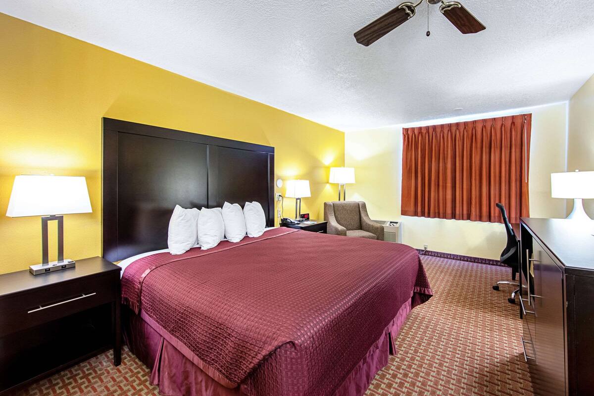 Hotelkamer met een groot bed, twee nachtkastjes met lampen, een bureau met stoel, een plafondventilator en een raam met gordijnen.